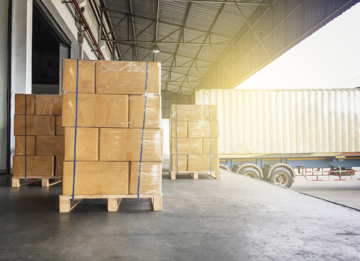 Warehouse cargo courier shipment. Stack of cardboard boxes on wooden pallet and truck docking at warehouse