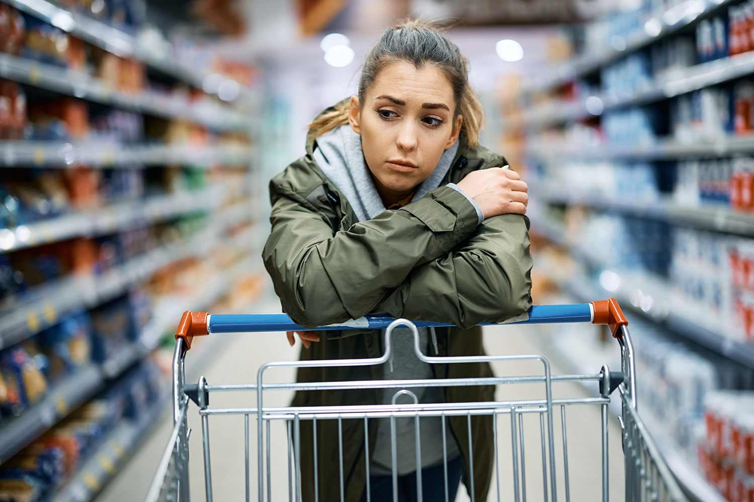 Young woman shopping in grocery store, leaning on cart